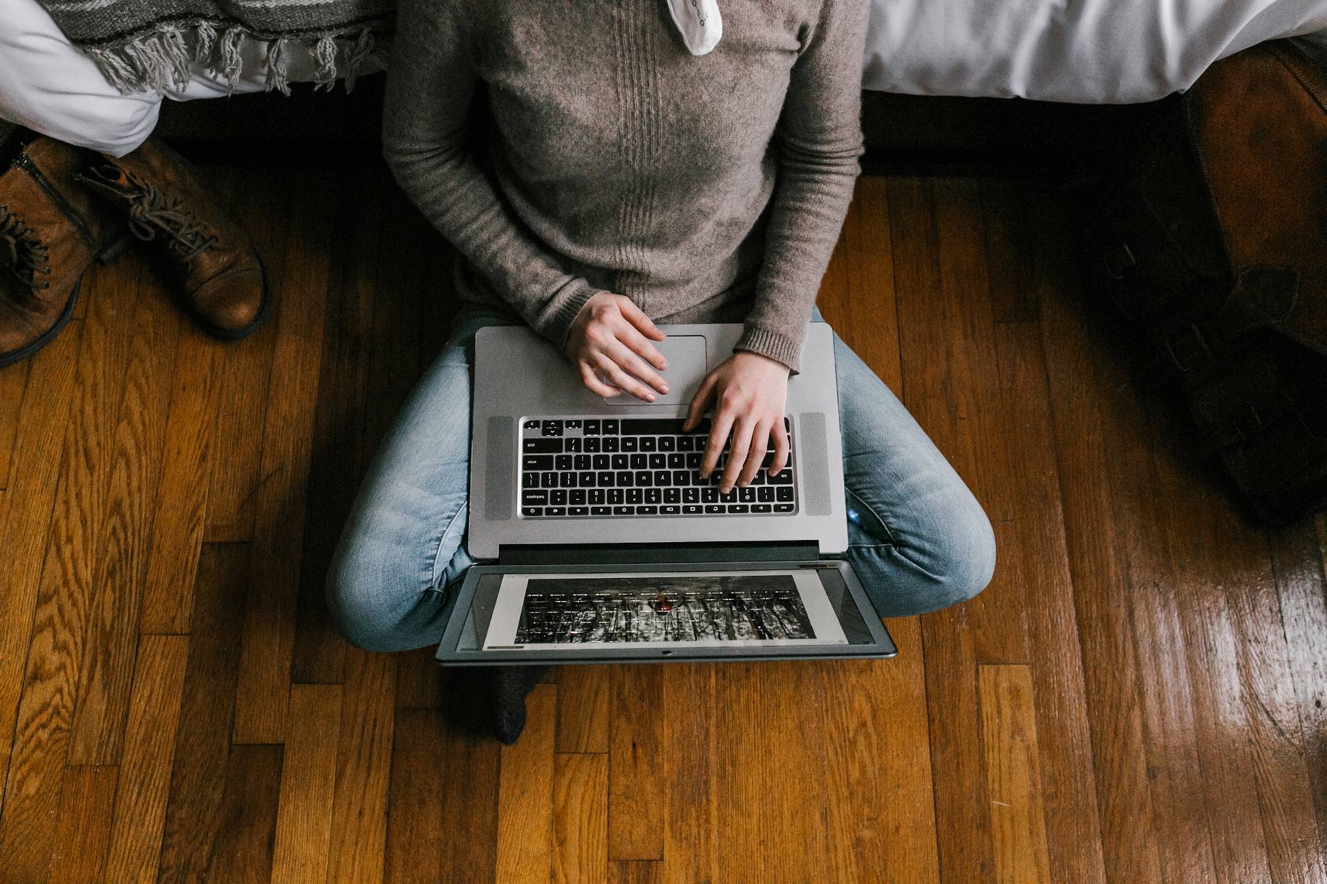 Woman working remotely on a laptop, sitting cross-legged on a hardwood floor. Ideal for remote work, productivity, and home office themes.