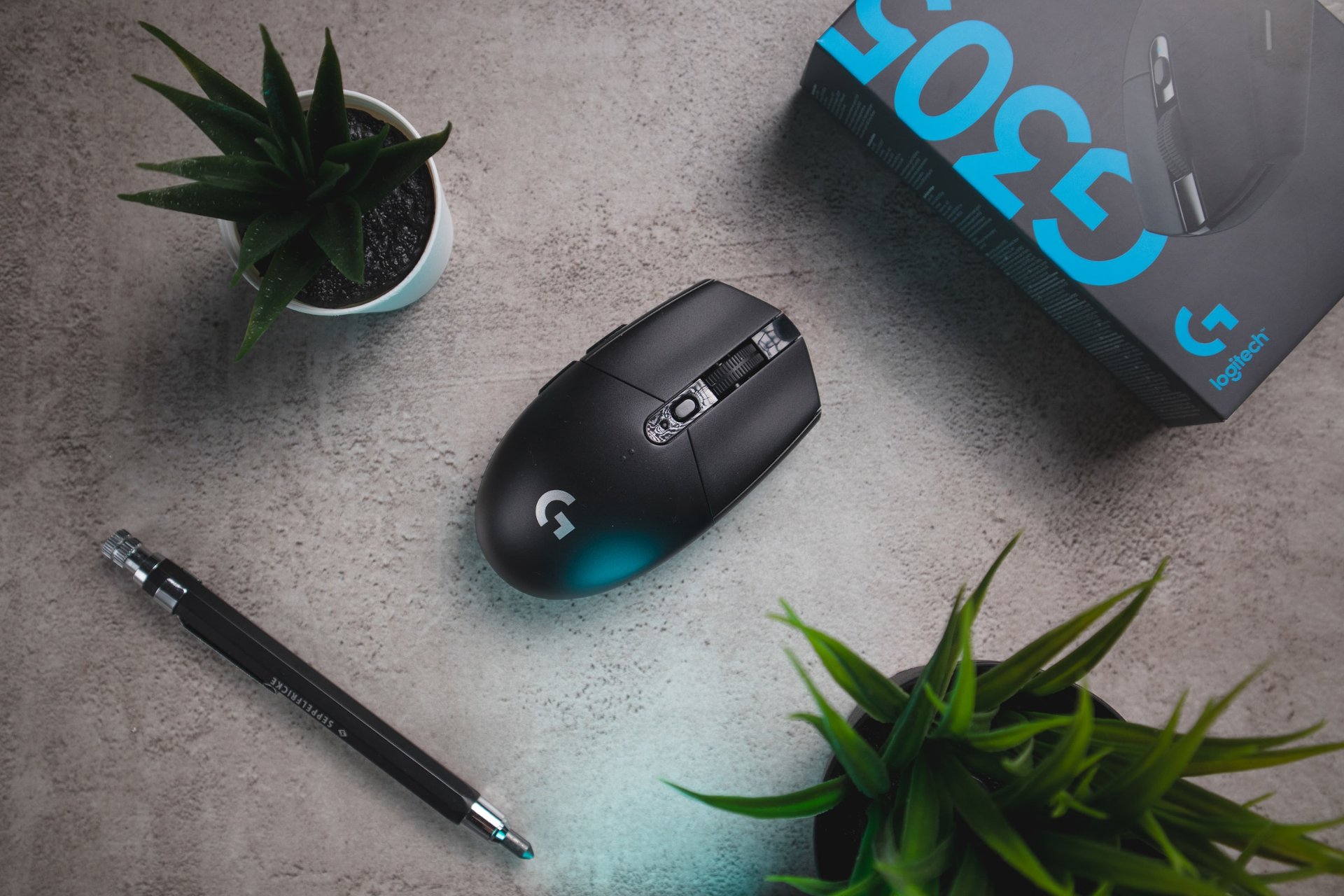 Logitech G502 gaming mouse on a textured surface with plants and a pen, showcasing its sleek design and packaging.