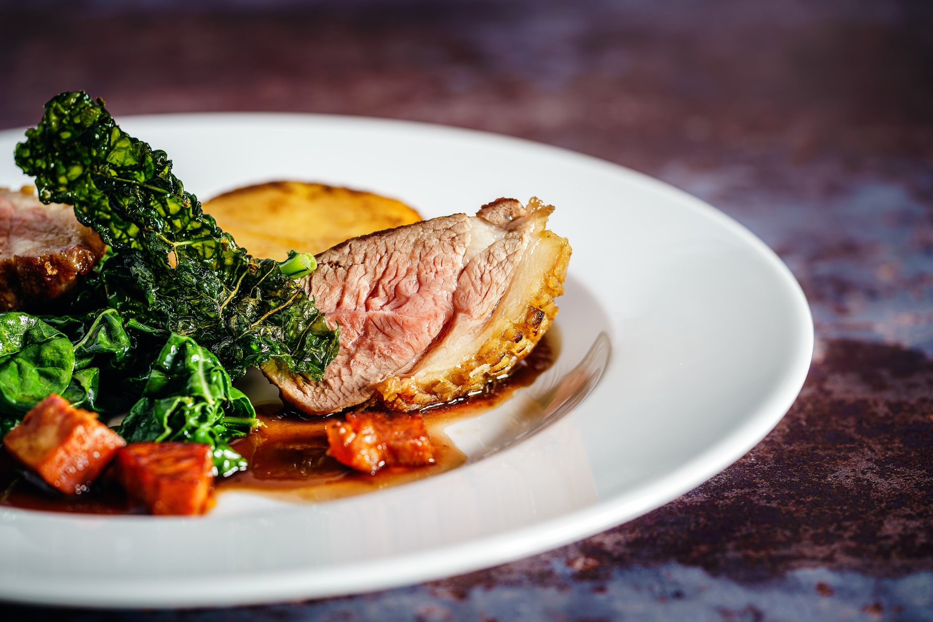 A gourmet dish featuring tender meat, sautéed greens, and crispy kale, elegantly plated for a fine dining experience.