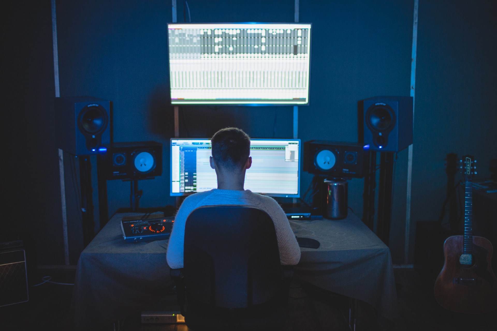 A person working in a modern music studio, focused on audio editing with multiple screens and speakers.